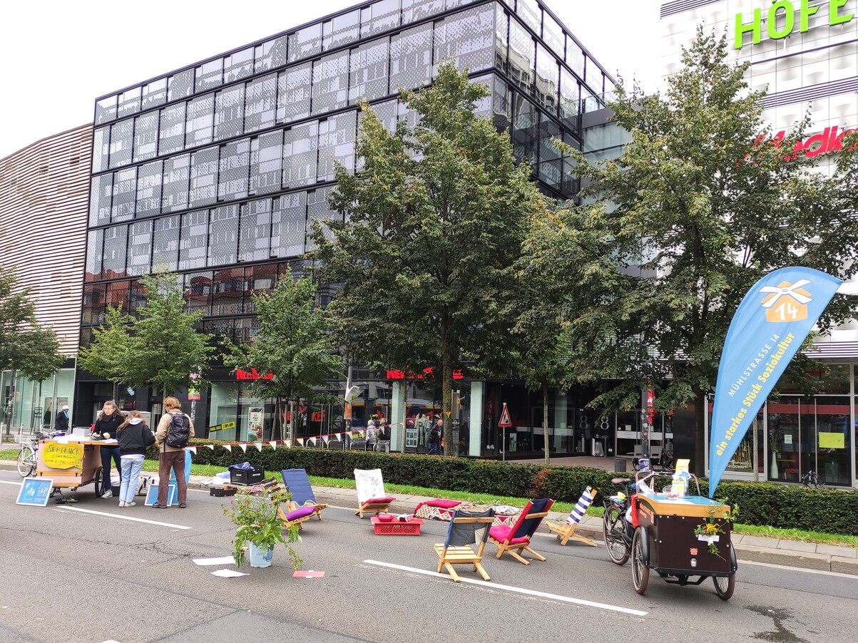 Es zeigt ein Lastenrad, Schwedenstühle und einen kleinen Tisch mit teppcih. Außerdem sit ein mobiler Stand zu sehen, der auf einem Schwerlast-Fahrrad-Anhänger zu sehen ist. Alles wurde mit dem Lastenrad transportiert.